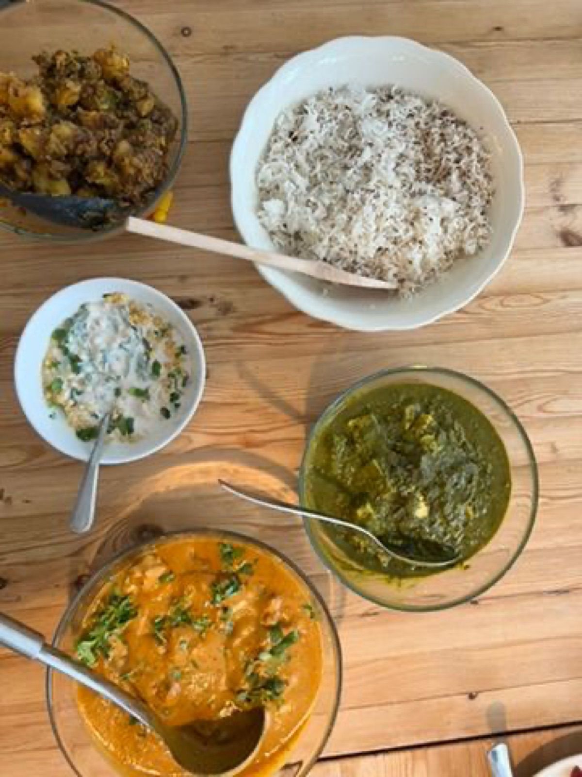 Butter chicken, saag paneer, rice, raita and aloo laid out on a wooden table